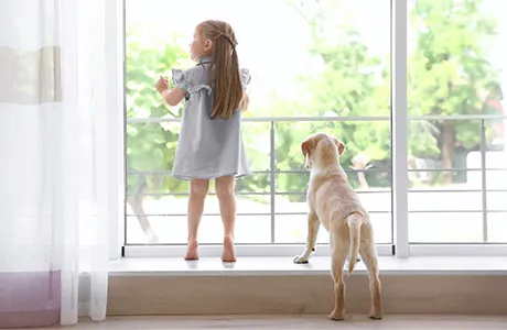young girl and puppy looking out large window.
